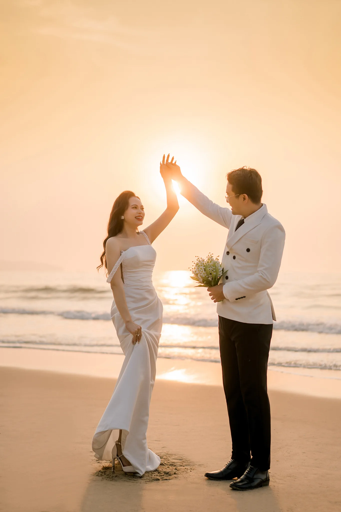 Cô dâu chú rể chạm lòng bàn tay vào nhau che đúng vầng mặt trời đang mọc trên biển