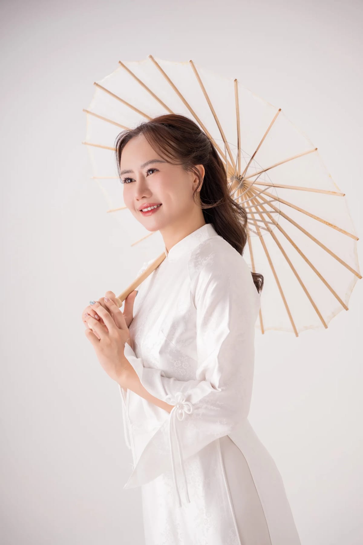 Cô gái mặc áo dài trắng cầm ô giấy, mỉm cười trên nền trắng
