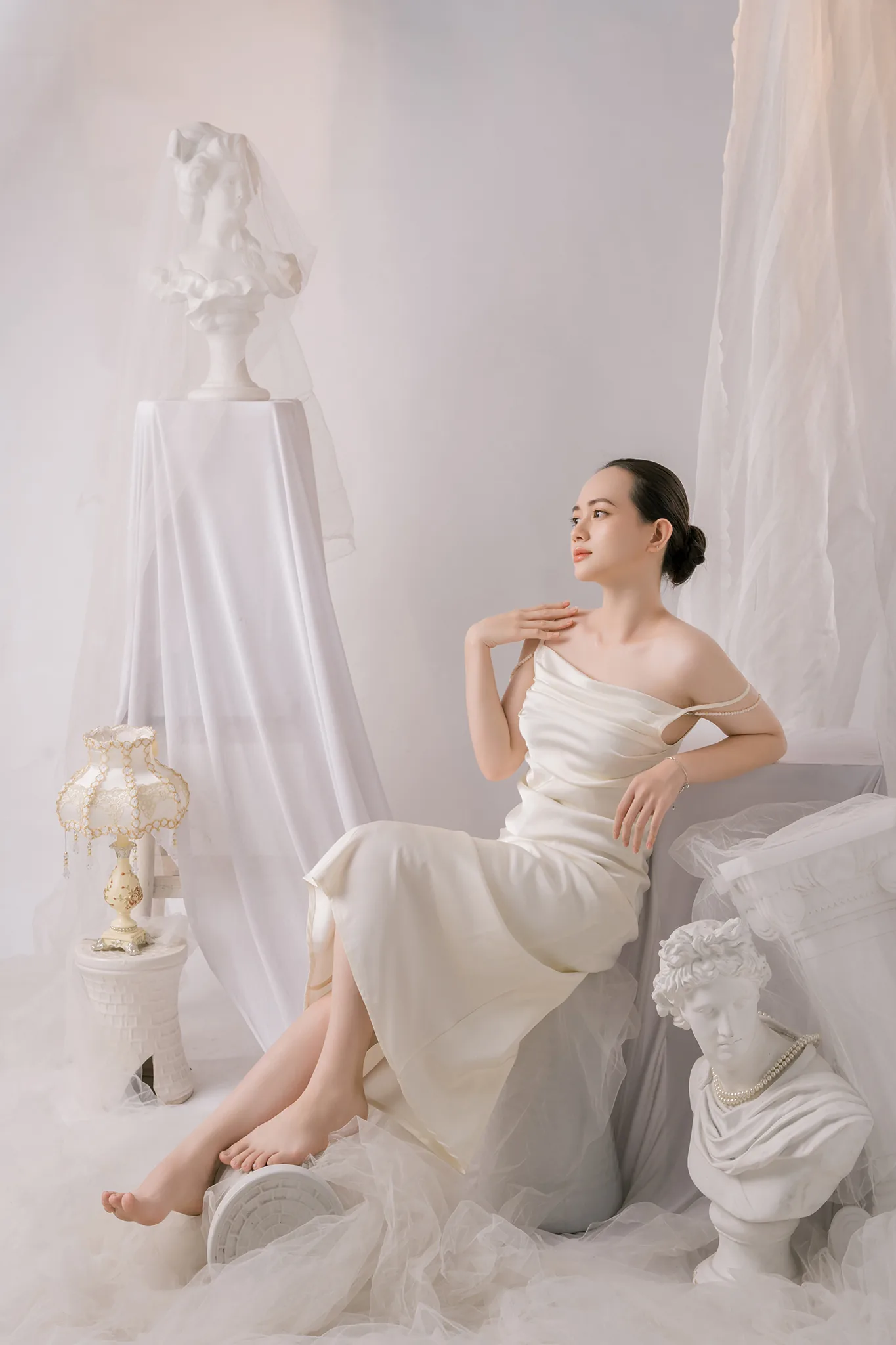 Cô gái váy lụa trắng ngả người tựa bục đá, nhìn về phía nguồn sáng