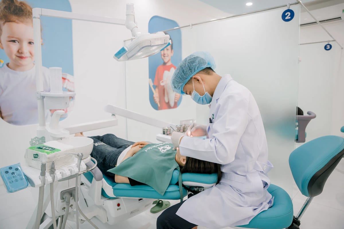 Bác sĩ làm việc tại khu ghế nha khoa trẻ em, tường trang trí hình các bé đang cầm bàn chải