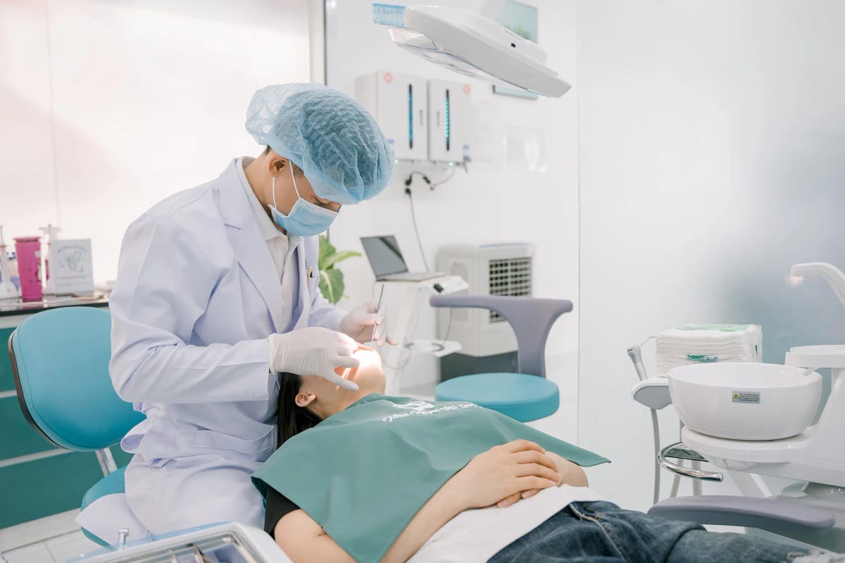 Bác sĩ nha khoa cúi người thao tác điều trị dưới ánh đèn, phòng khám ngập ánh sáng tự nhiên
