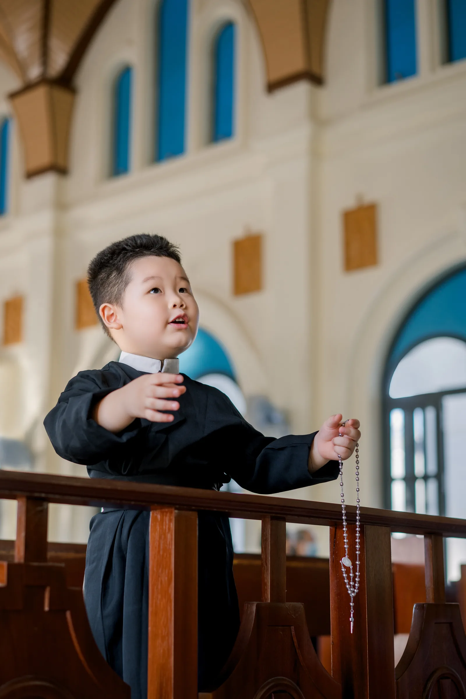 Cậu bé mặc áo chùng thâm cổ trắng, một tay áp ngực, tay kia cầm chuỗi mân côi, ngẩng lên hát trong lòng nhà thờ